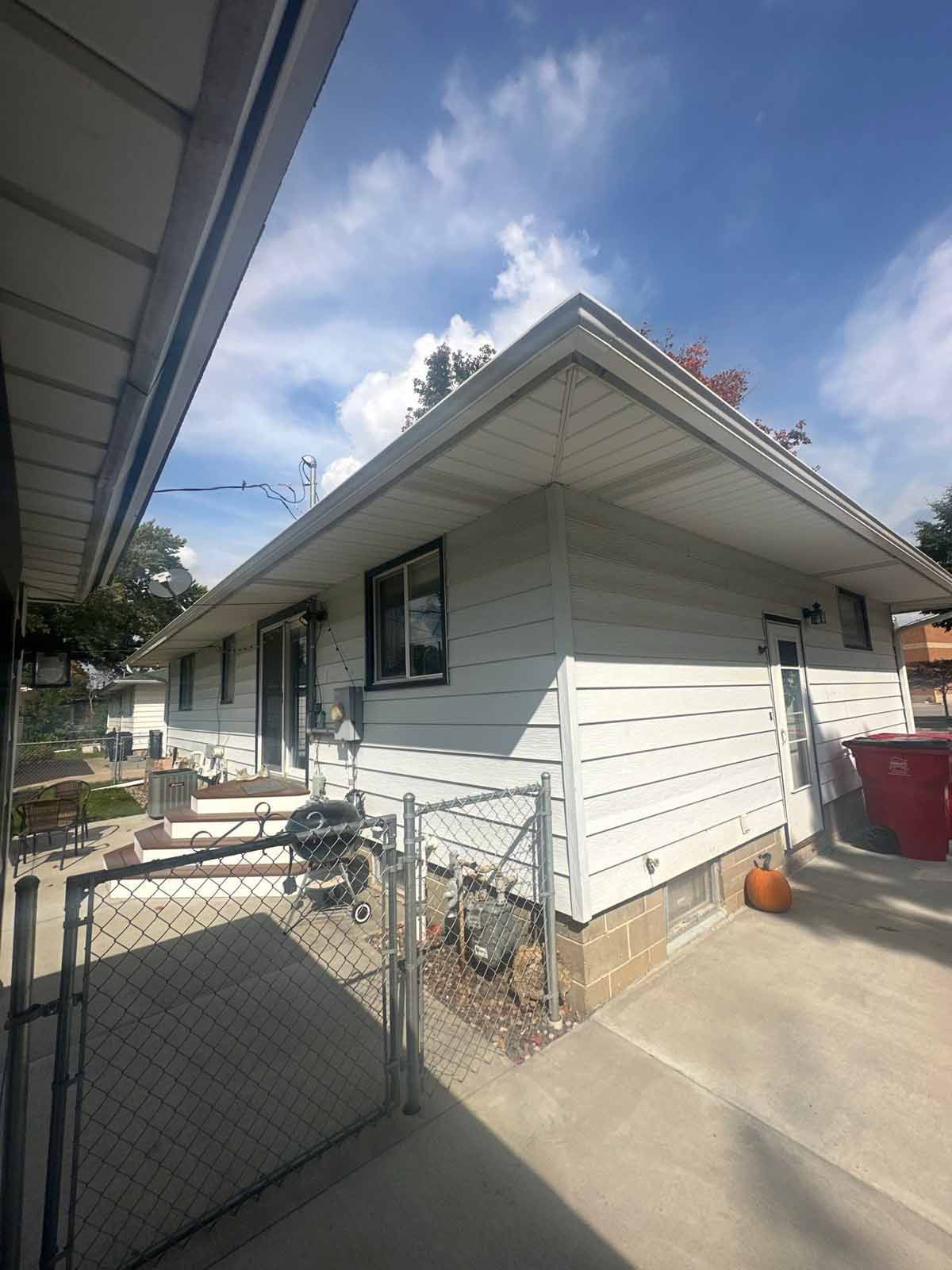 White house with a gray roof and a chain-link fence on a sunny day.