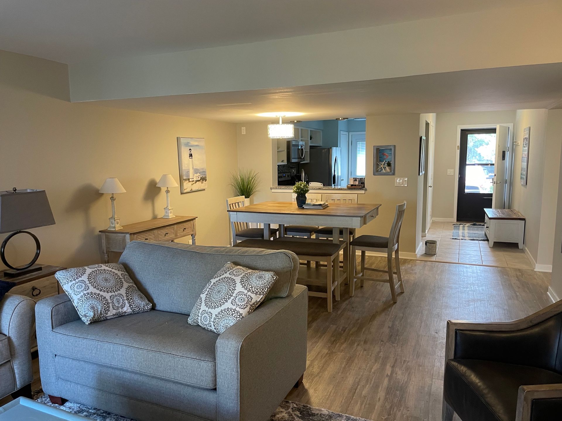Cozy living room with open kitchen. Gray sofa, neutral walls, dining table, and dark front door.