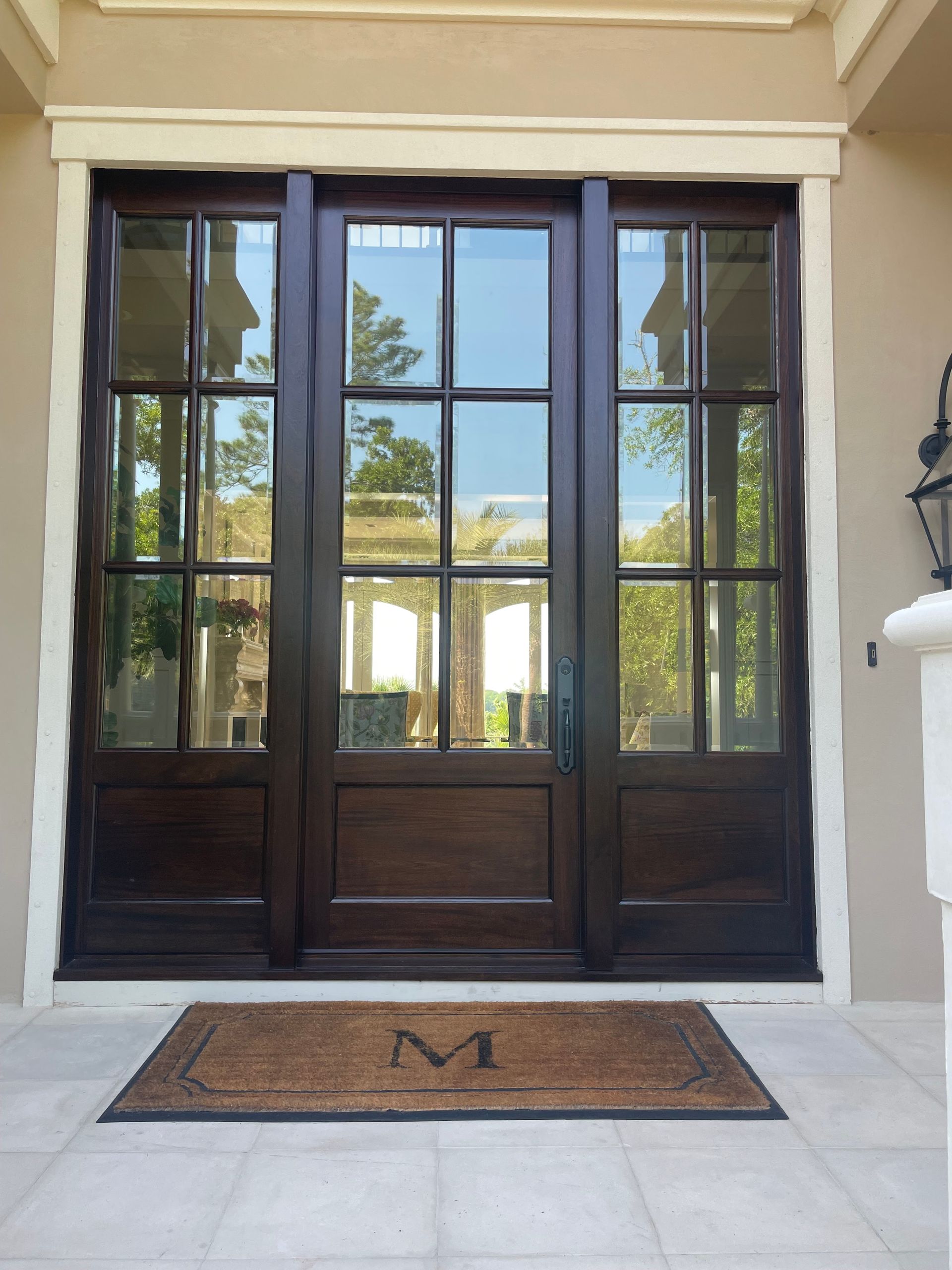 Dark wood front door with glass panels; mat with the letter 