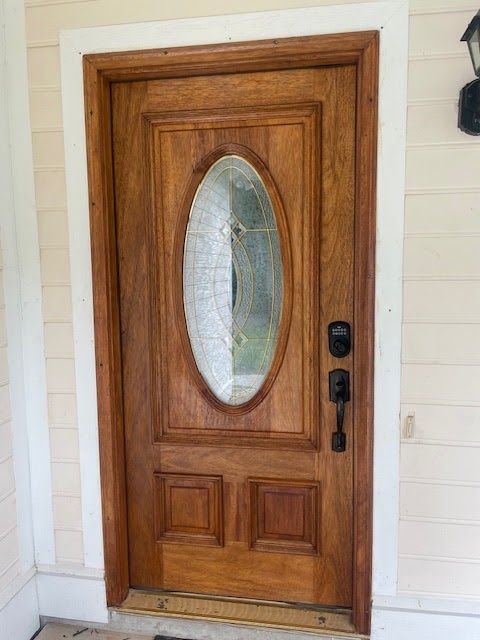 Wooden door with oval glass pane, brown finish, black hardware, set in a beige frame.