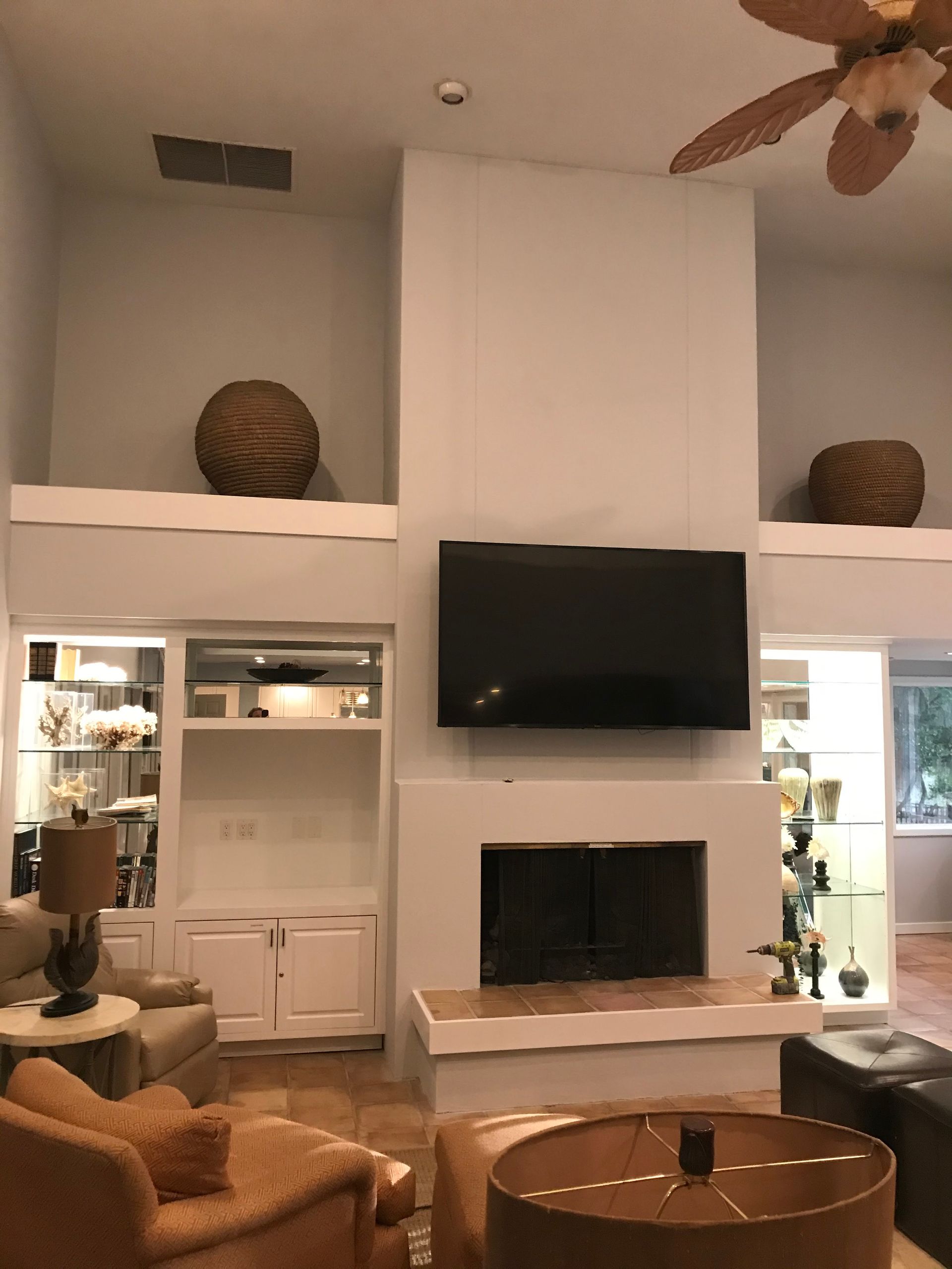 Living room with high ceilings, fireplace, TV, built-in shelving, and decorative woven spheres.