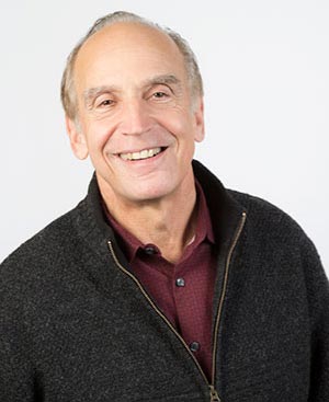 A man wearing a black jacket and a red shirt is smiling for the camera.