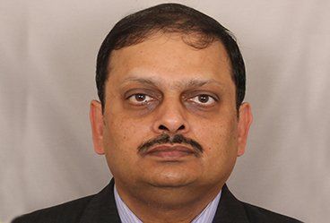 A man with a mustache is wearing a suit and tie and looking at the camera.