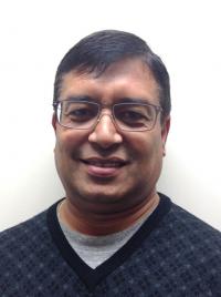 A man wearing glasses and a sweater is smiling for the camera.