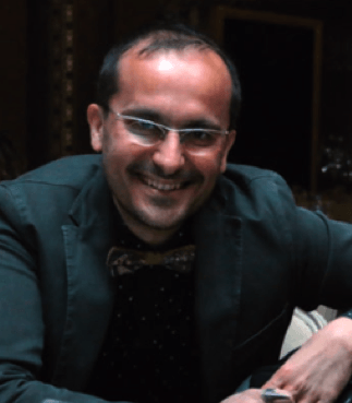 A man wearing glasses and a bow tie smiles for the camera