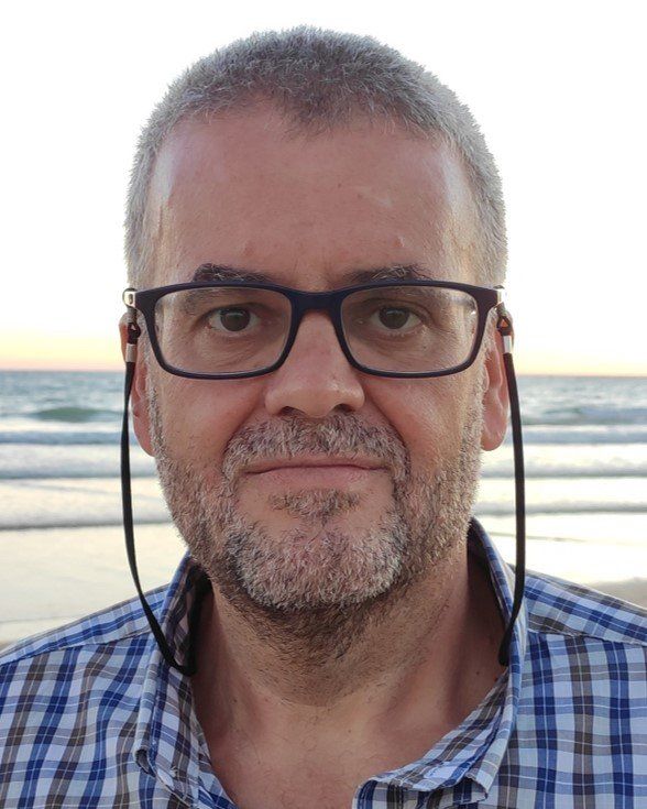 A man wearing glasses and headphones is standing on a beach.