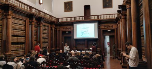 A group of people are sitting in front of a projector screen in a library.