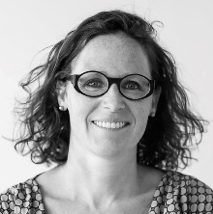 A woman wearing glasses and a polka dot shirt is smiling in a black and white photo.