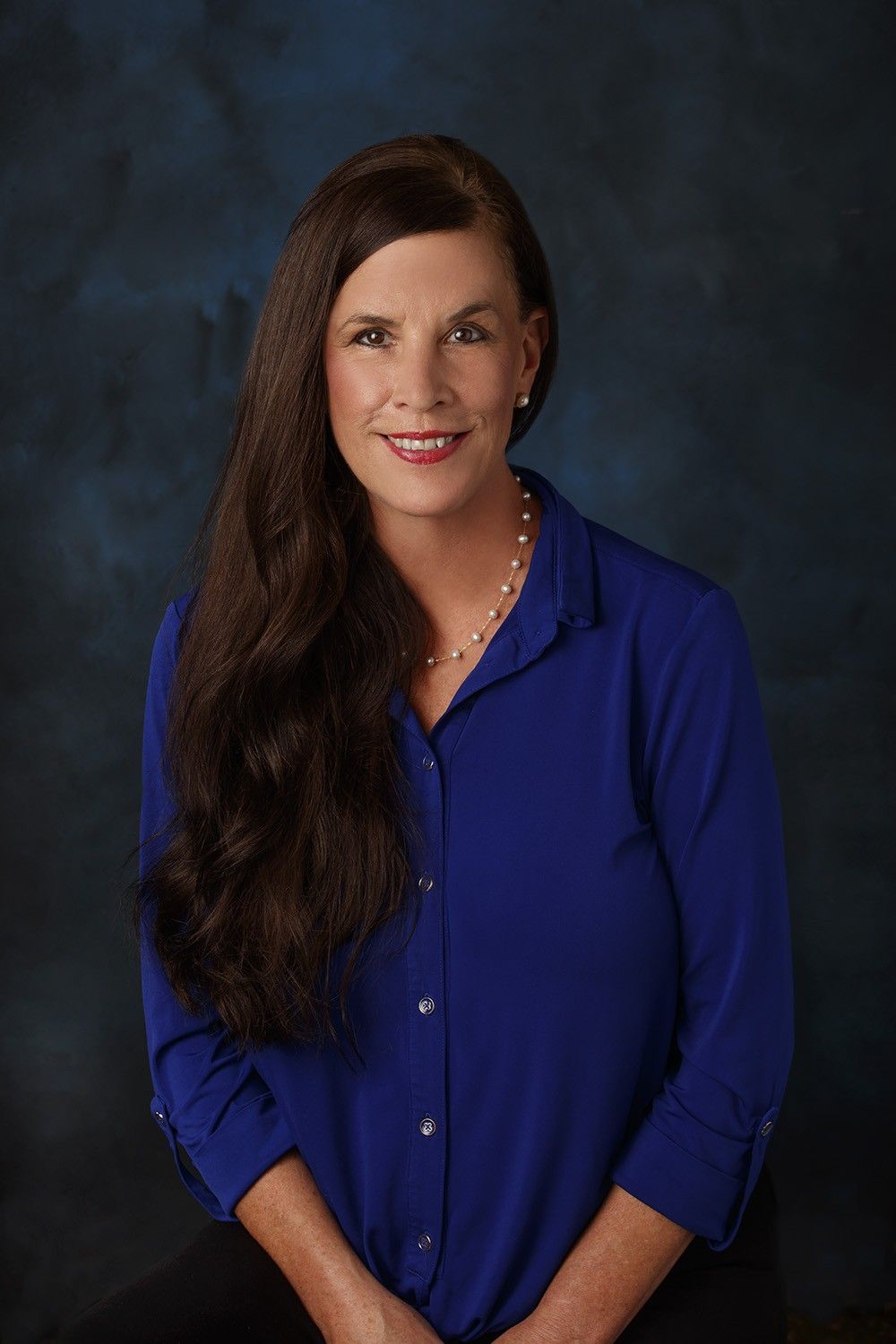 The woman is wearing a blue shirt and a pearl necklace.