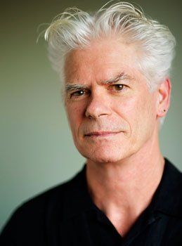 A man with white hair is wearing a black shirt and looking at the camera.