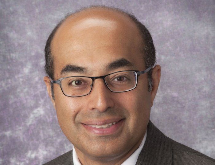 A bald man wearing glasses and a suit smiles for the camera