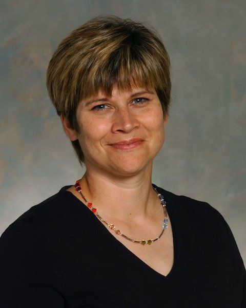 A woman wearing a black shirt and a necklace smiles for the camera