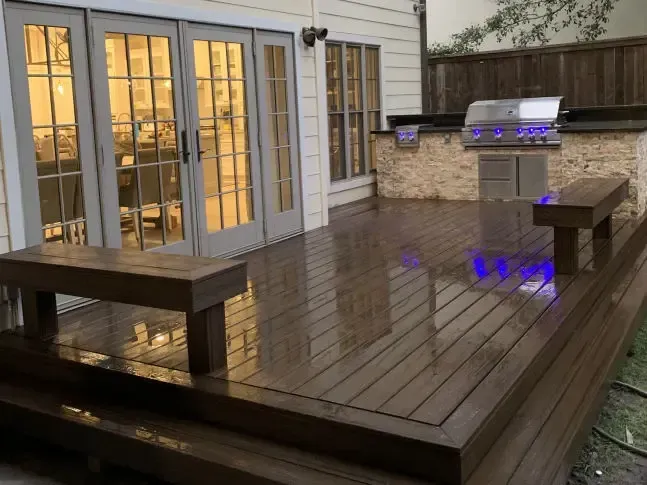 A wooden deck with a grill and benches in front of a house.
