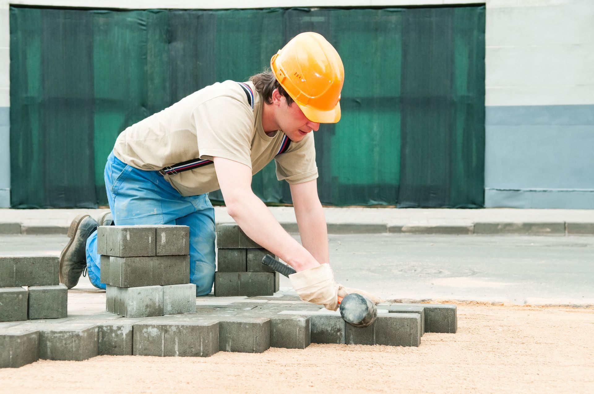 A man wearing a hard hat is laying bricks on the ground.