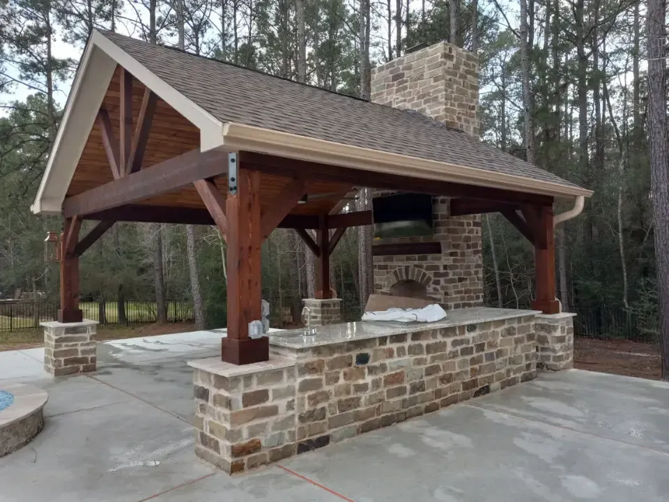 A brick pavilion with a wooden roof and a fireplace.