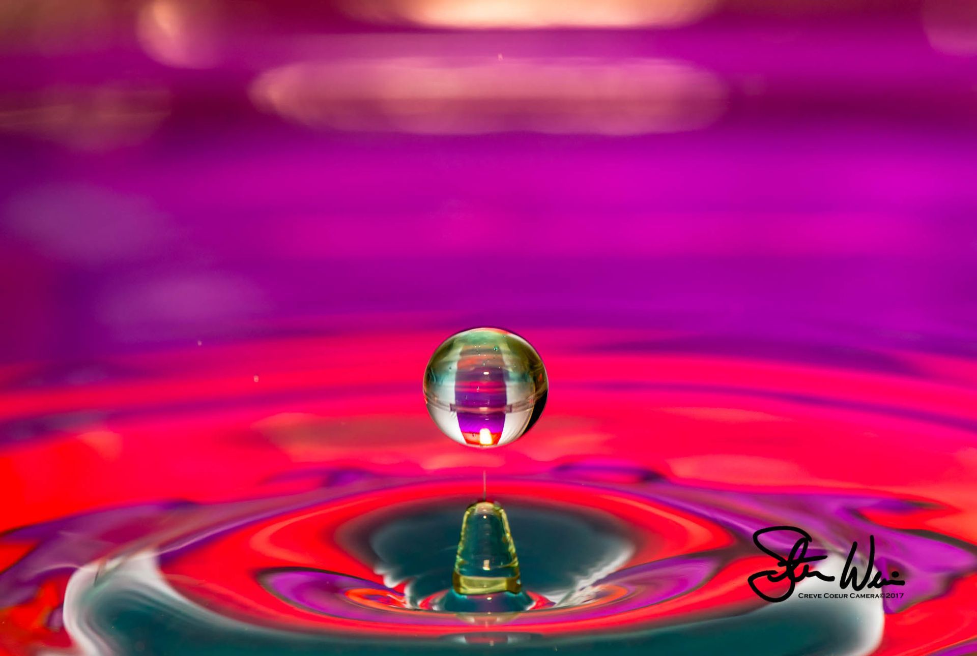 a drop of water is floating in a purple and red liquid .