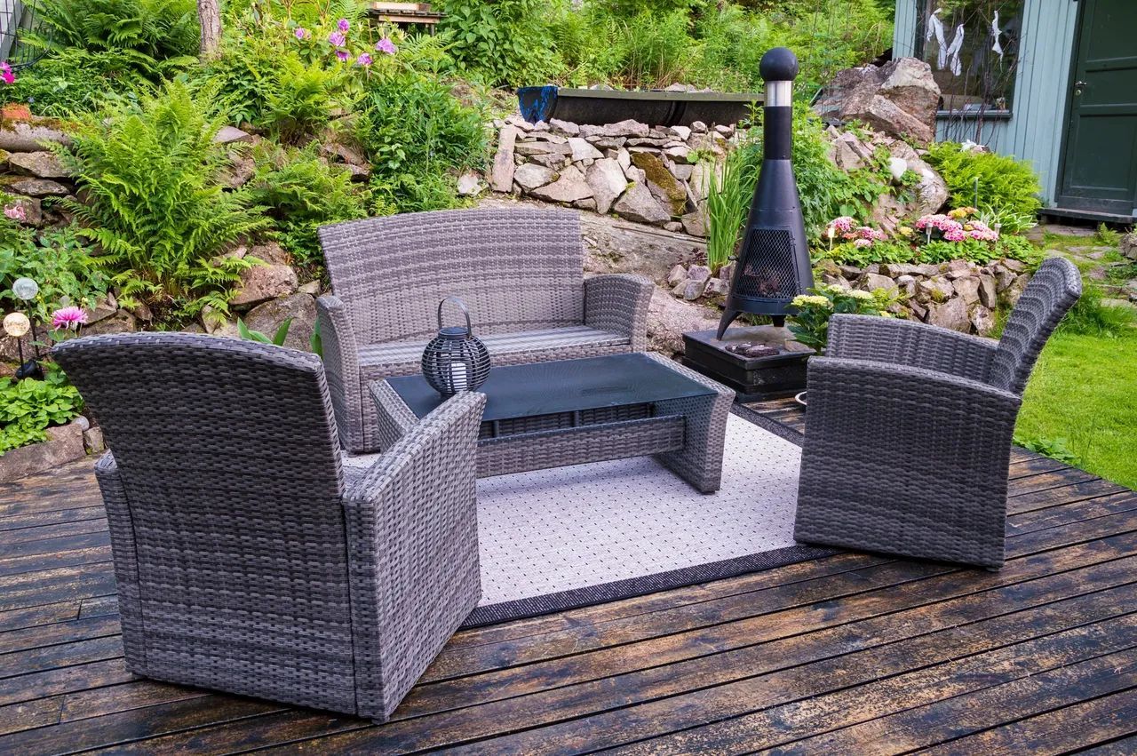 A wicker patio set is sitting on a wooden deck in a garden.