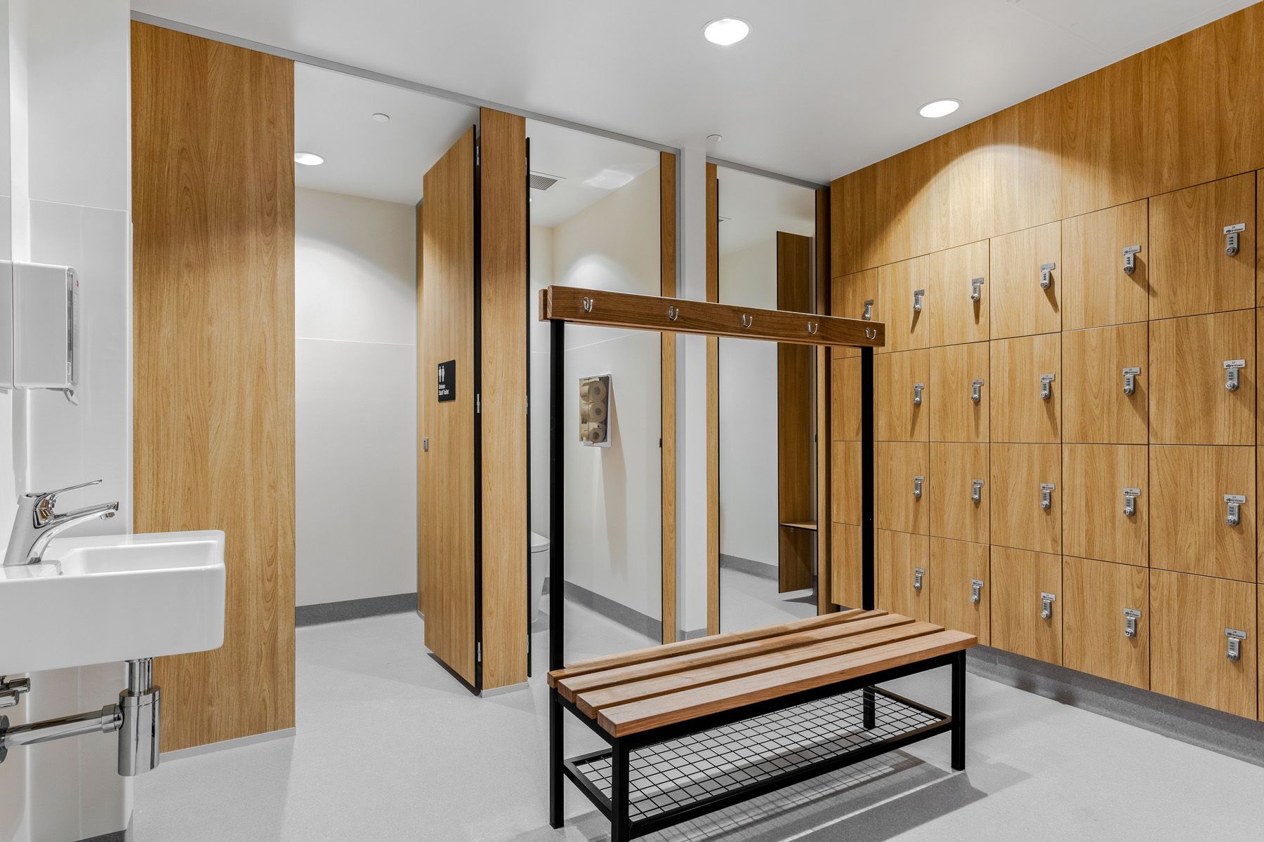 A locker room with wooden lockers , a bench , a sink and mirrors.