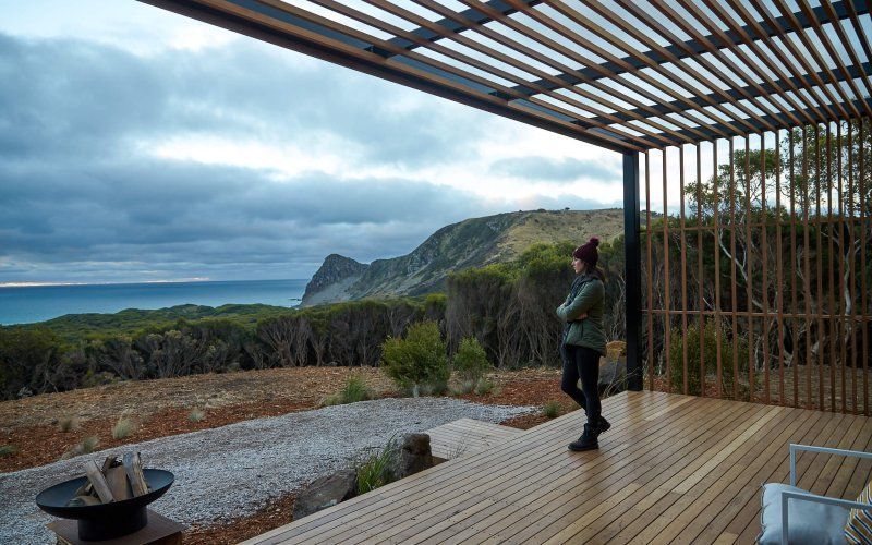 A woman is standing on a wooden deck overlooking the ocean.