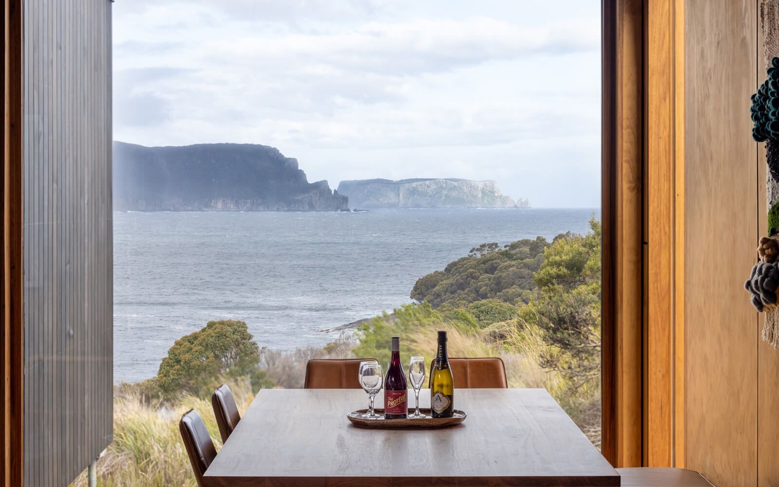 A dining room table with bottles of wine on it and a view of the ocean.