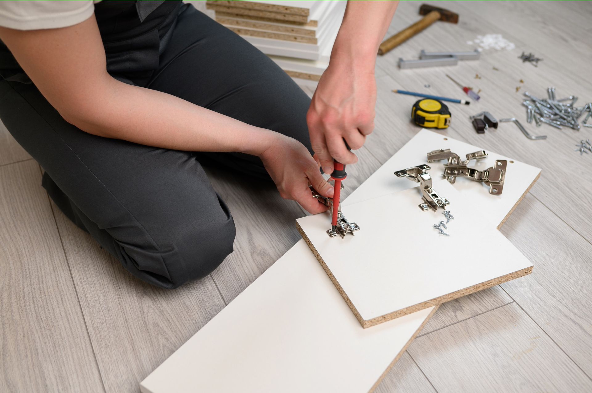 Person assembling furniture, using a screwdriver to attach hinges to a white cabinet door.