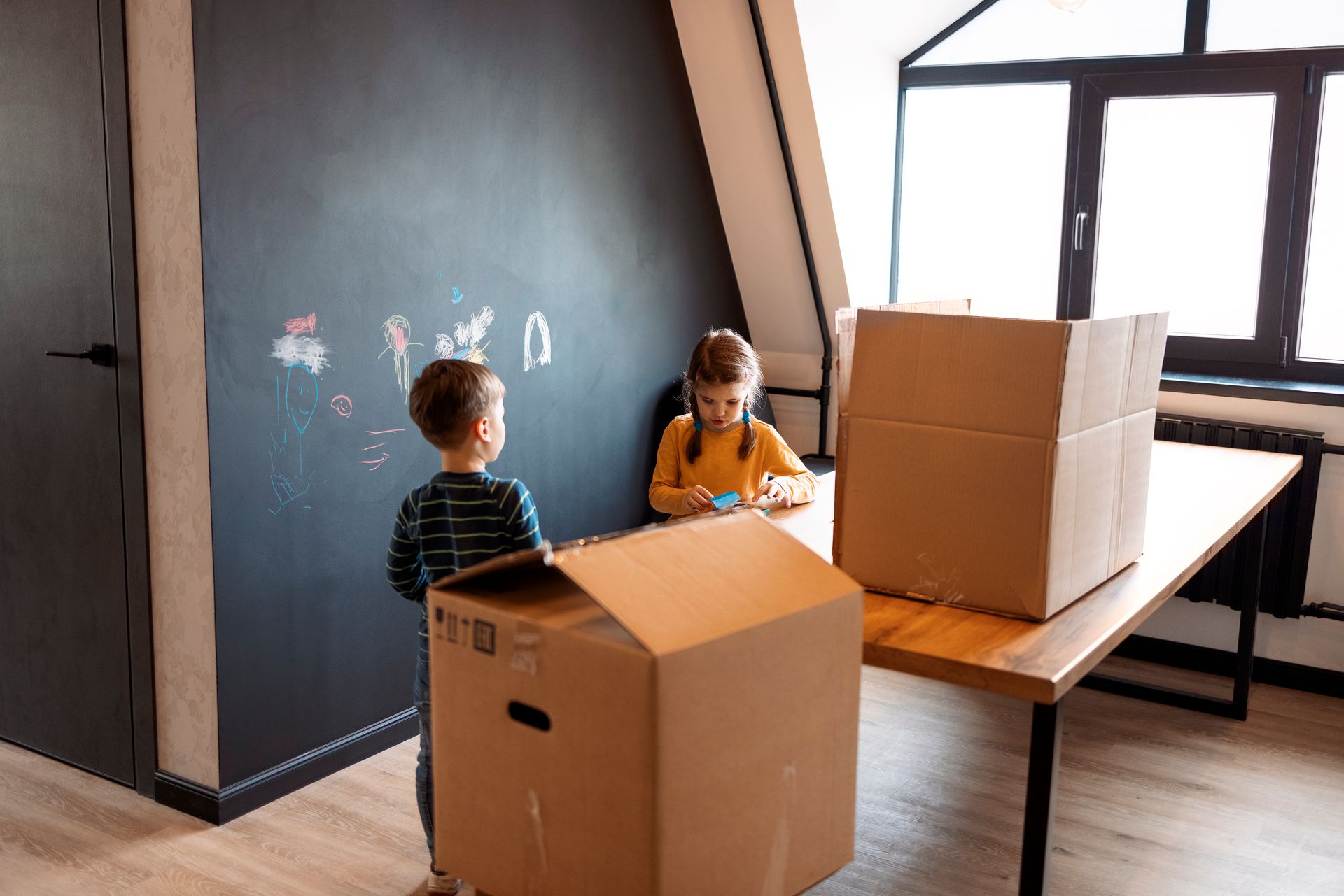 Two children are playing with cardboard boxes in a room.