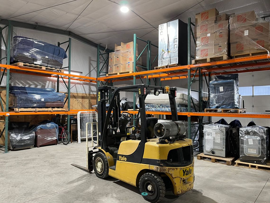 A yellow forklift is parked in a large warehouse filled with shelves and boxes.