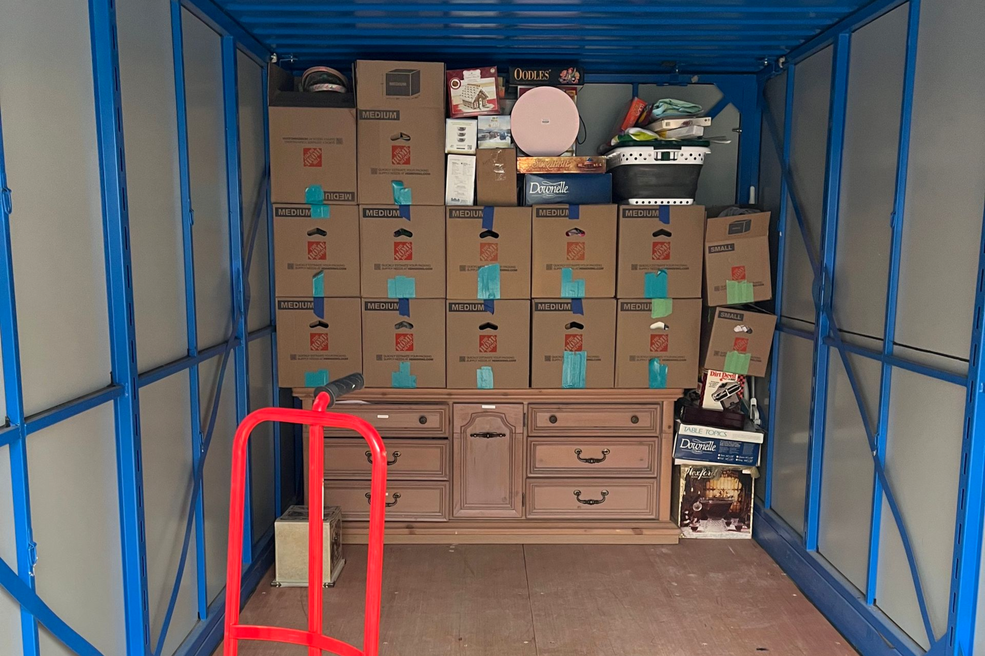 Couple wrapping couch in plastic during a move. Light-colored sofa, light wood floor, bright room.