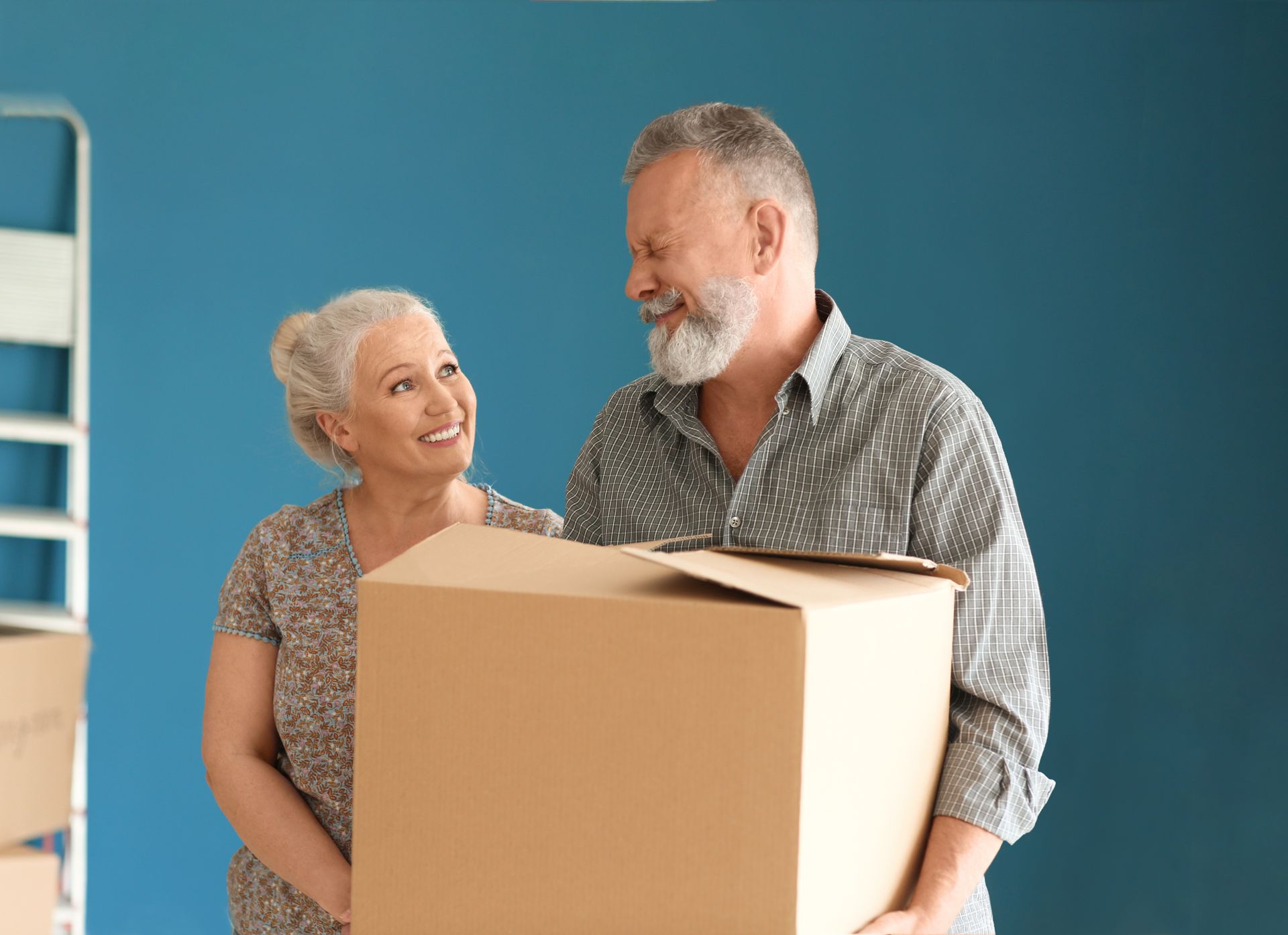 A man and a woman are holding a cardboard box in a room.