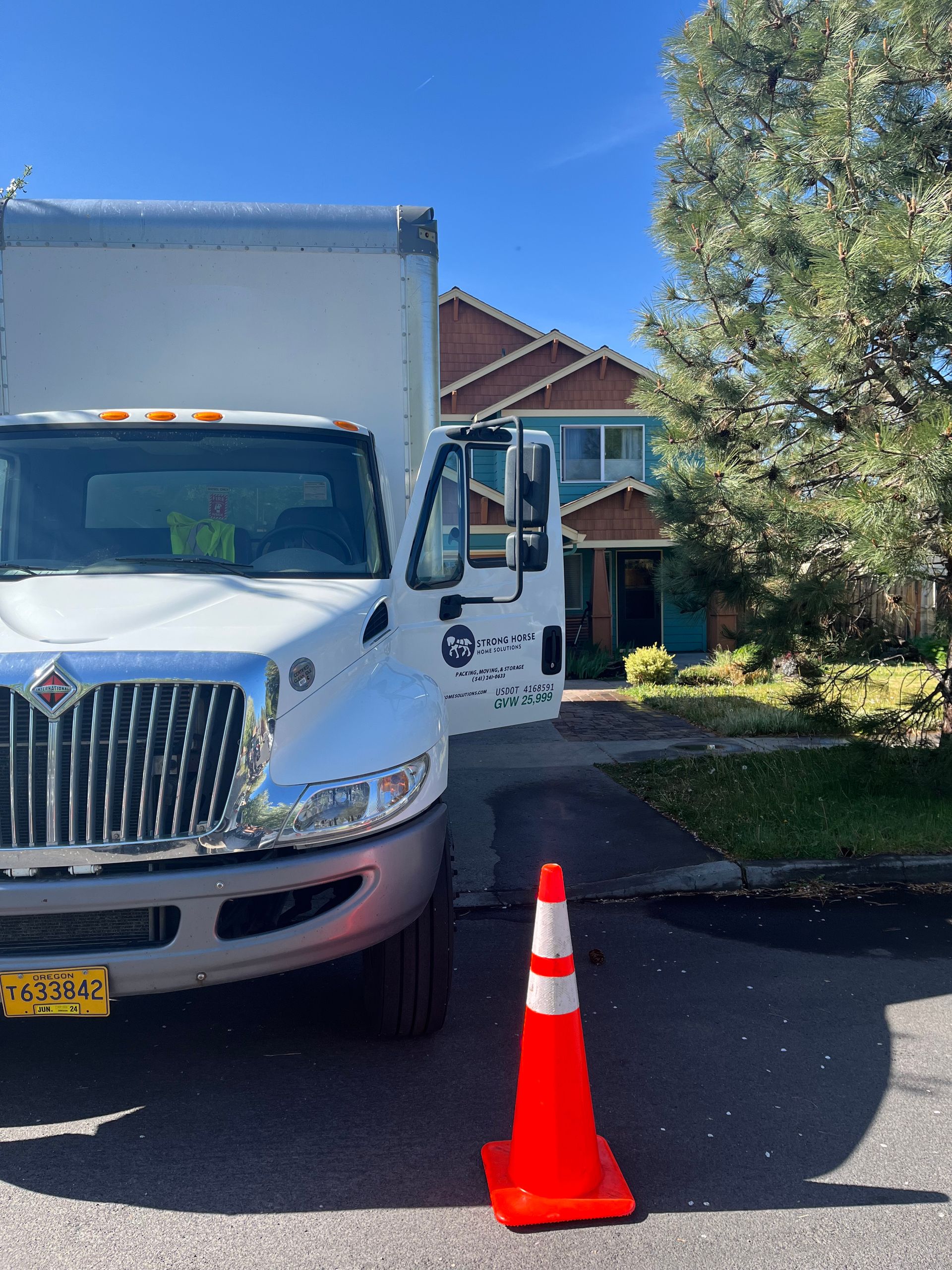 White truck parked on a street with a traffic cone in front. House in the background. Blue sky.