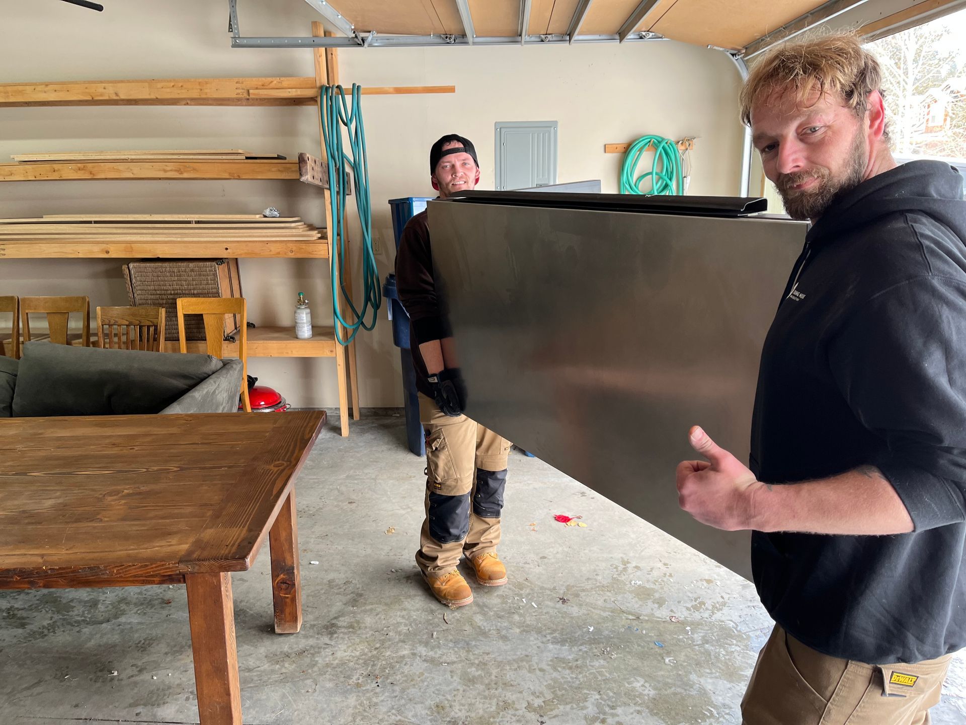 Two men are carrying a large piece of metal in a garage.