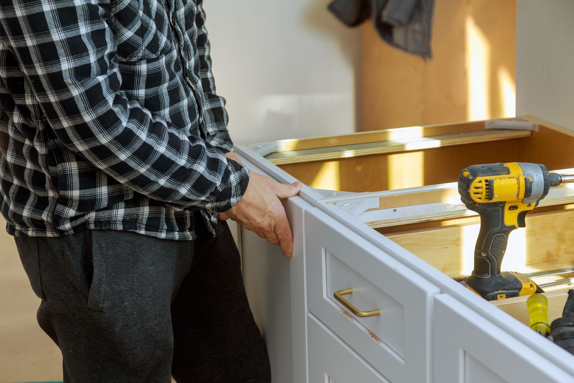Person installing white cabinet with a yellow power drill.