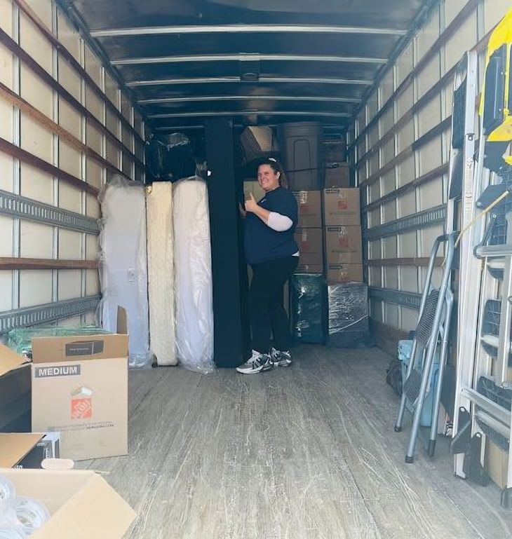 A red dolly is sitting inside of a blue container filled with boxes.