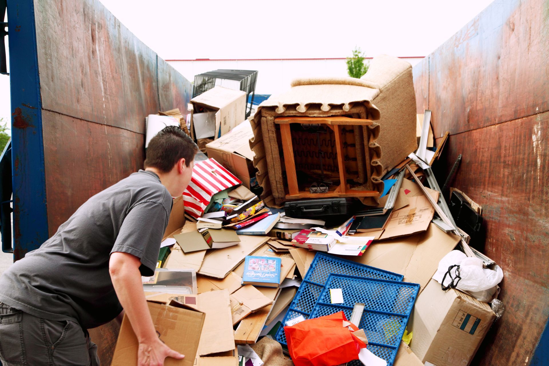 Man looks into a full dumpster with cardboard boxes and debris.