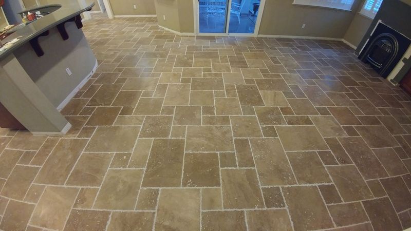 Brown tiled floor in a room, with a kitchen island on the left and a sliding glass door in the back.