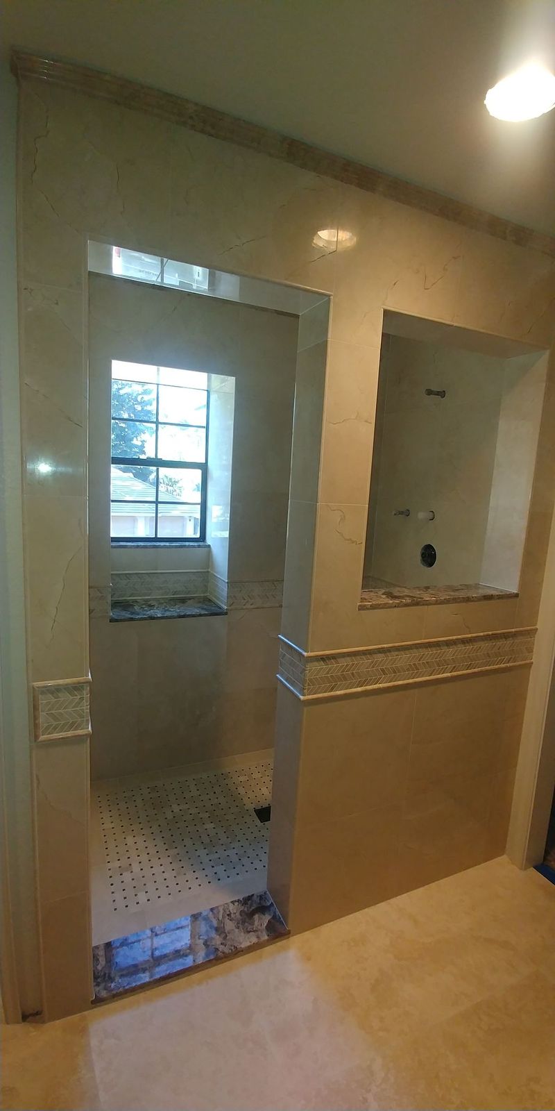 Bathroom with light-colored tile walls and floor, shower entrance, built-in shelf, and window.
