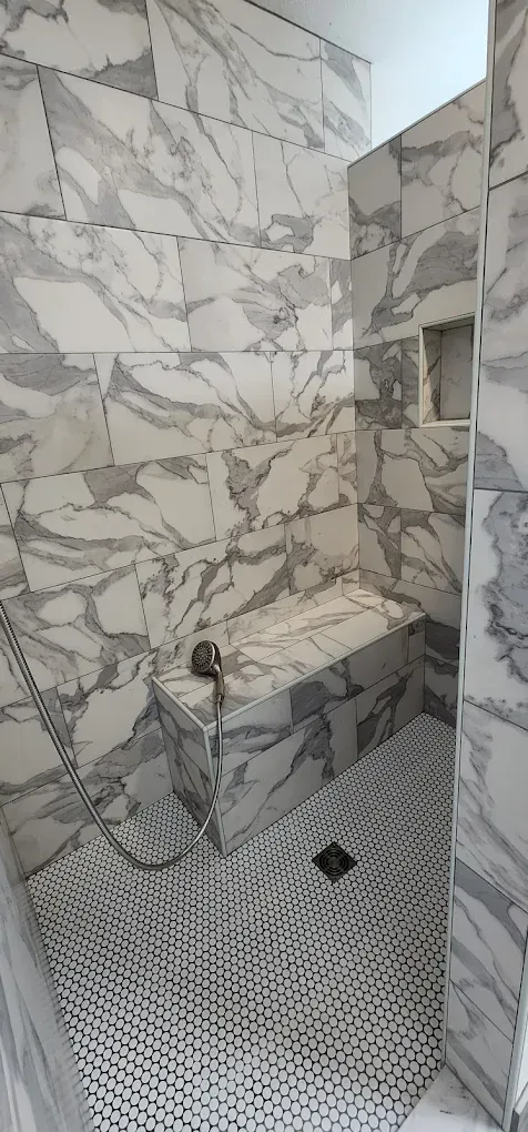 A shower with marble tiles and a bench in it.