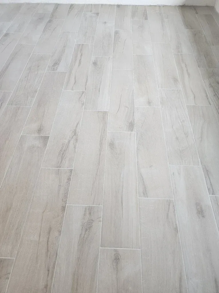 A close up of a white tile floor that looks like wood.