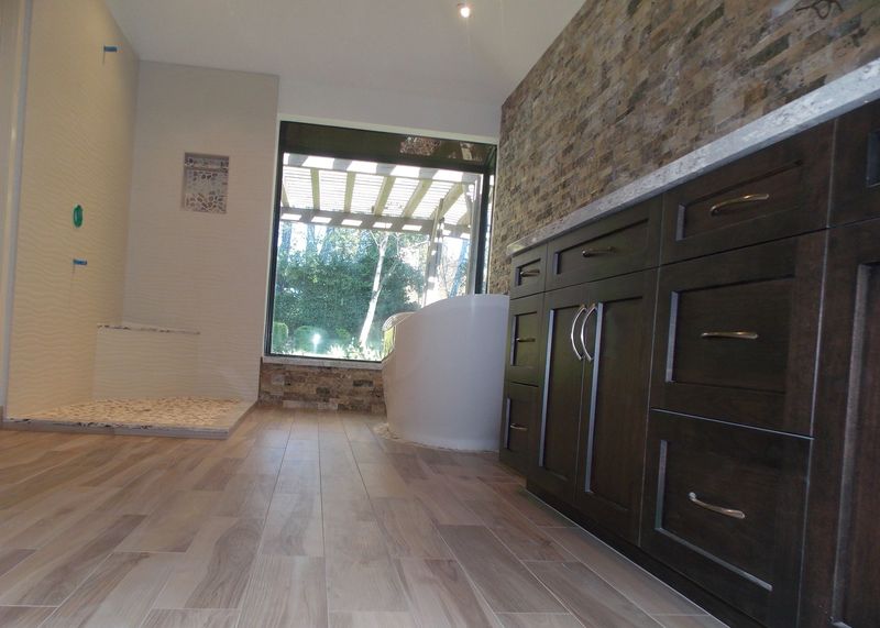 Bathroom with stone wall, dark cabinets, window, and light-colored flooring.