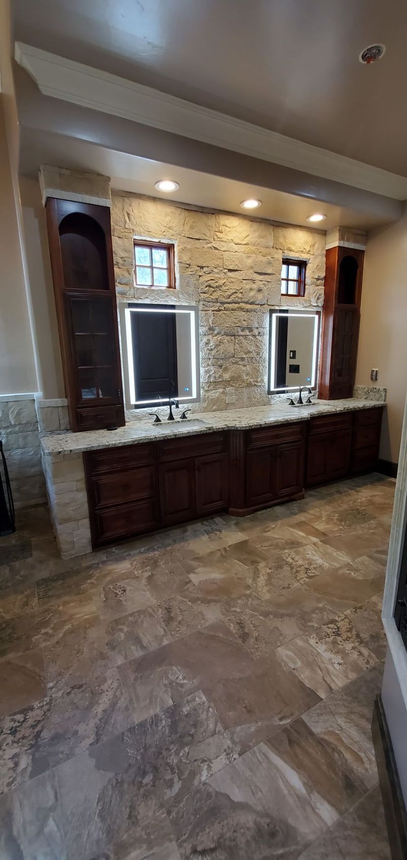 Bathroom with double vanity, dark cabinets, stone backsplash, and tile floor.