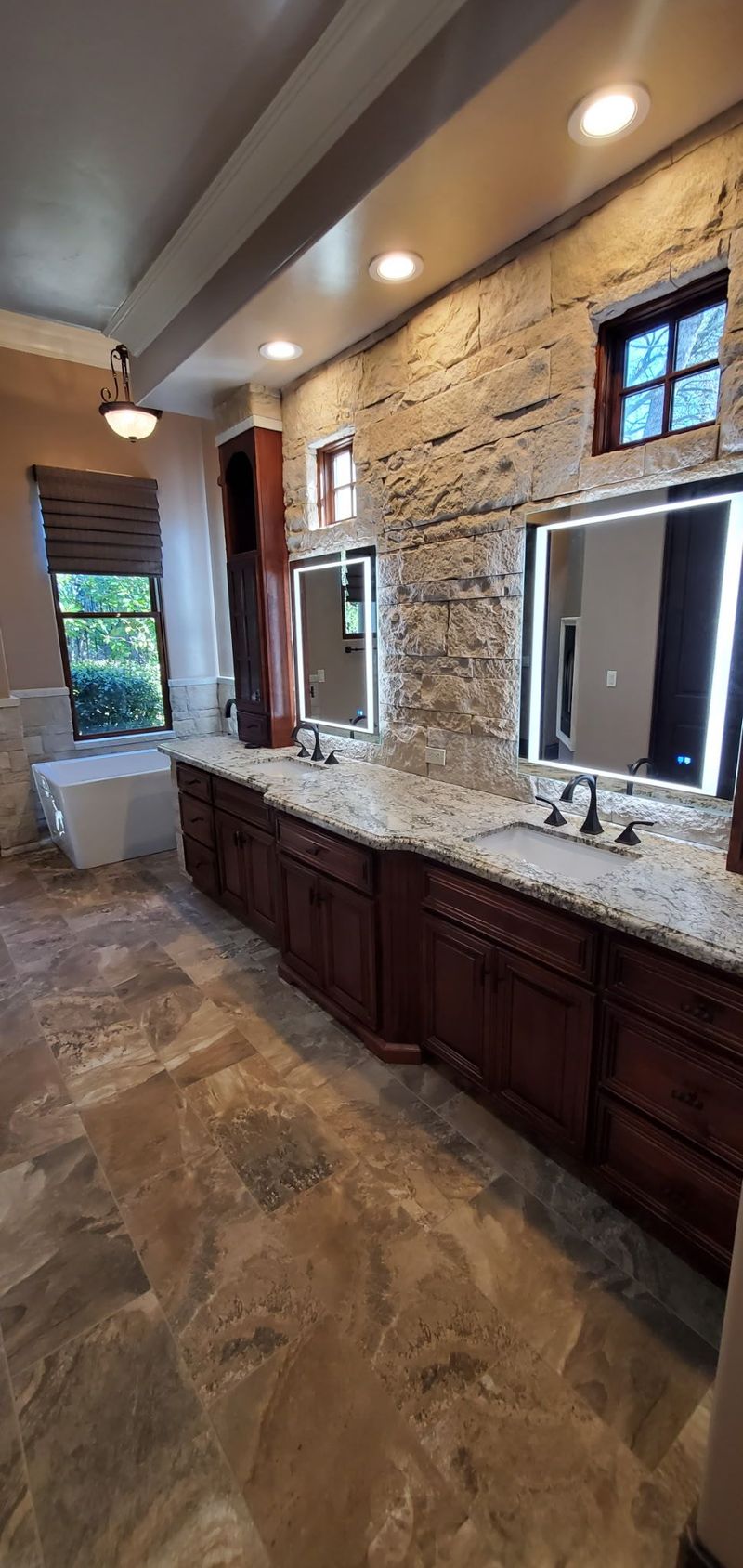 Bathroom with a stone accent wall, dark wood vanity, granite countertop, and large mirrors.