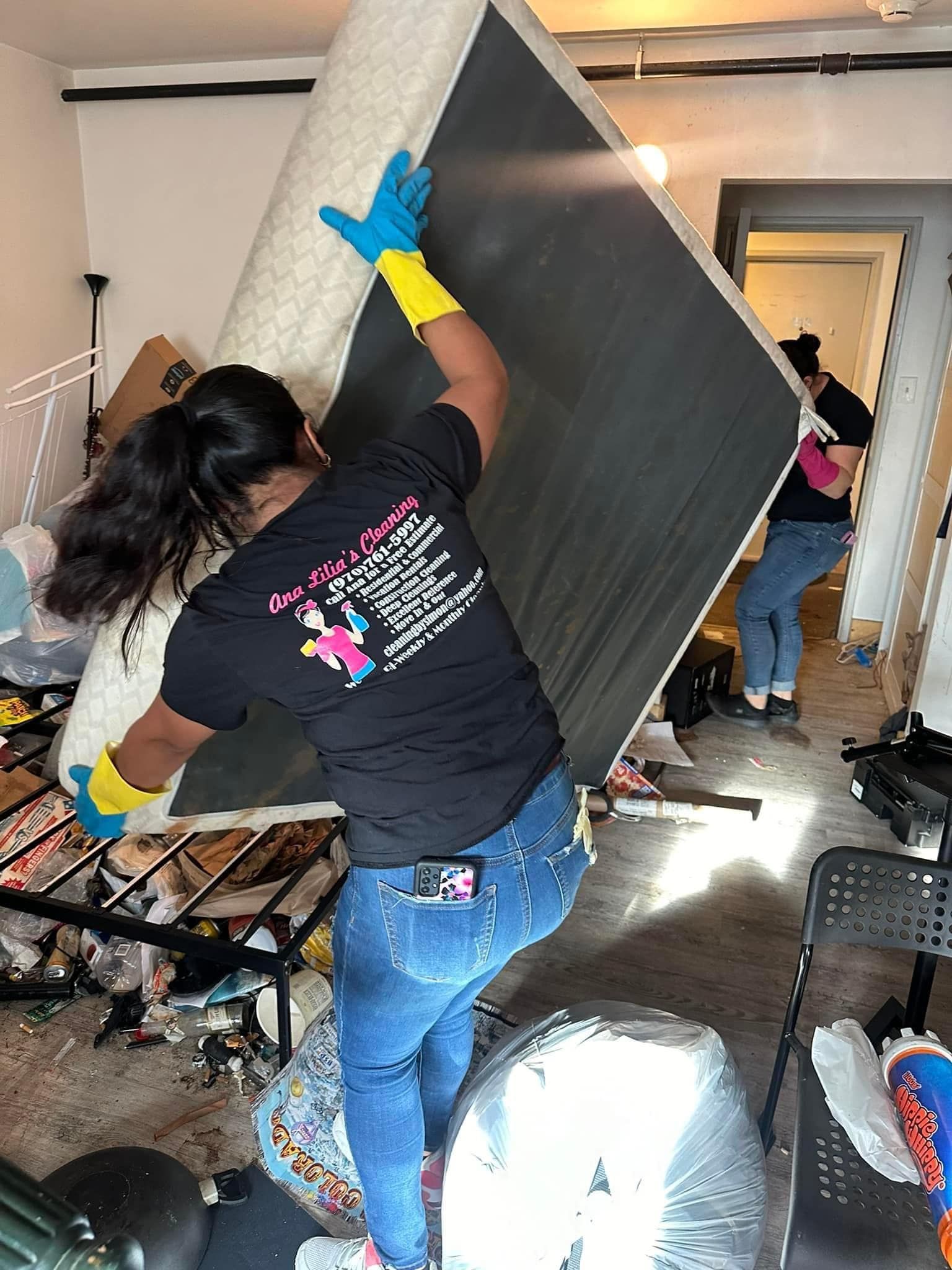 A woman is carrying a mattress in a messy room.