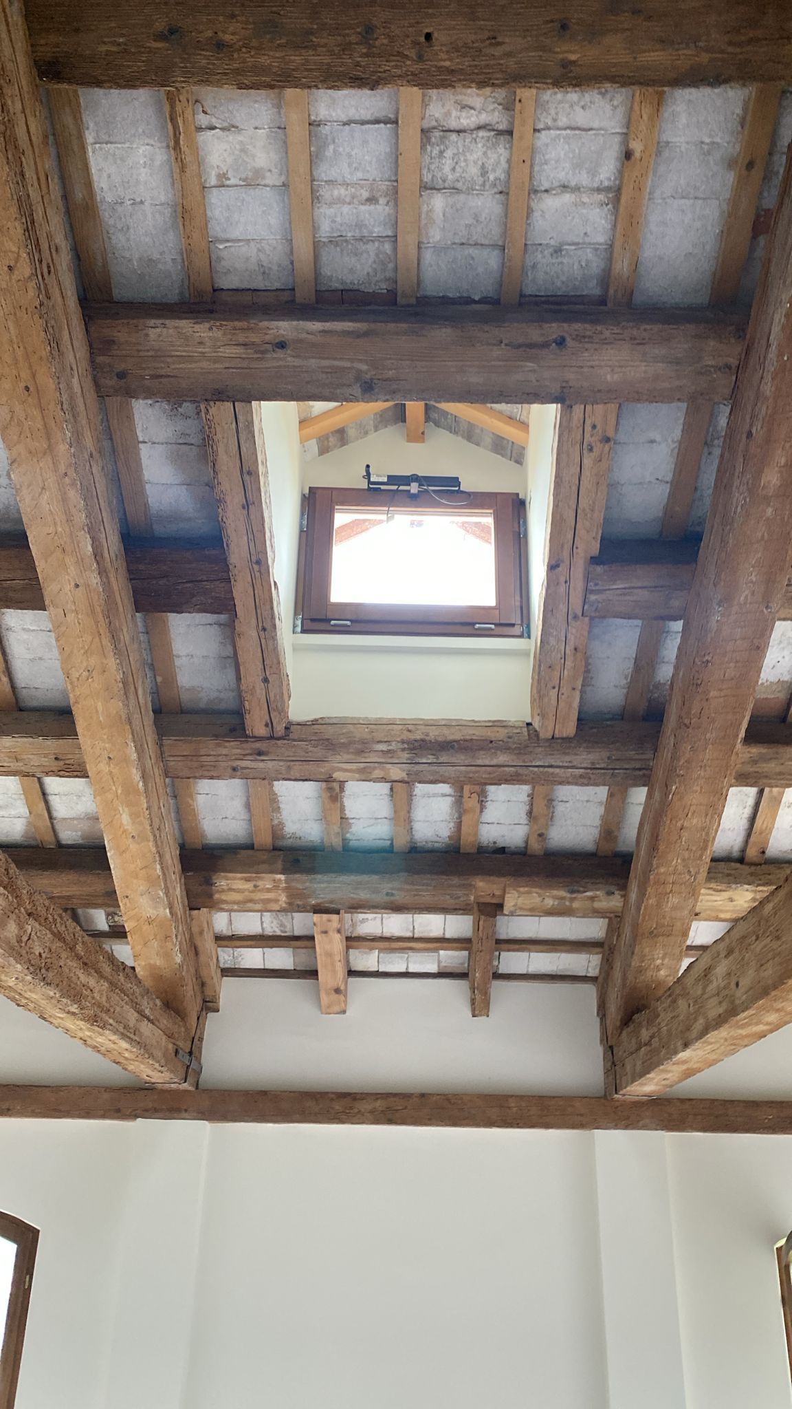 Guardando in alto verso il soffitto di un edificio con travi in legno e una finestra.