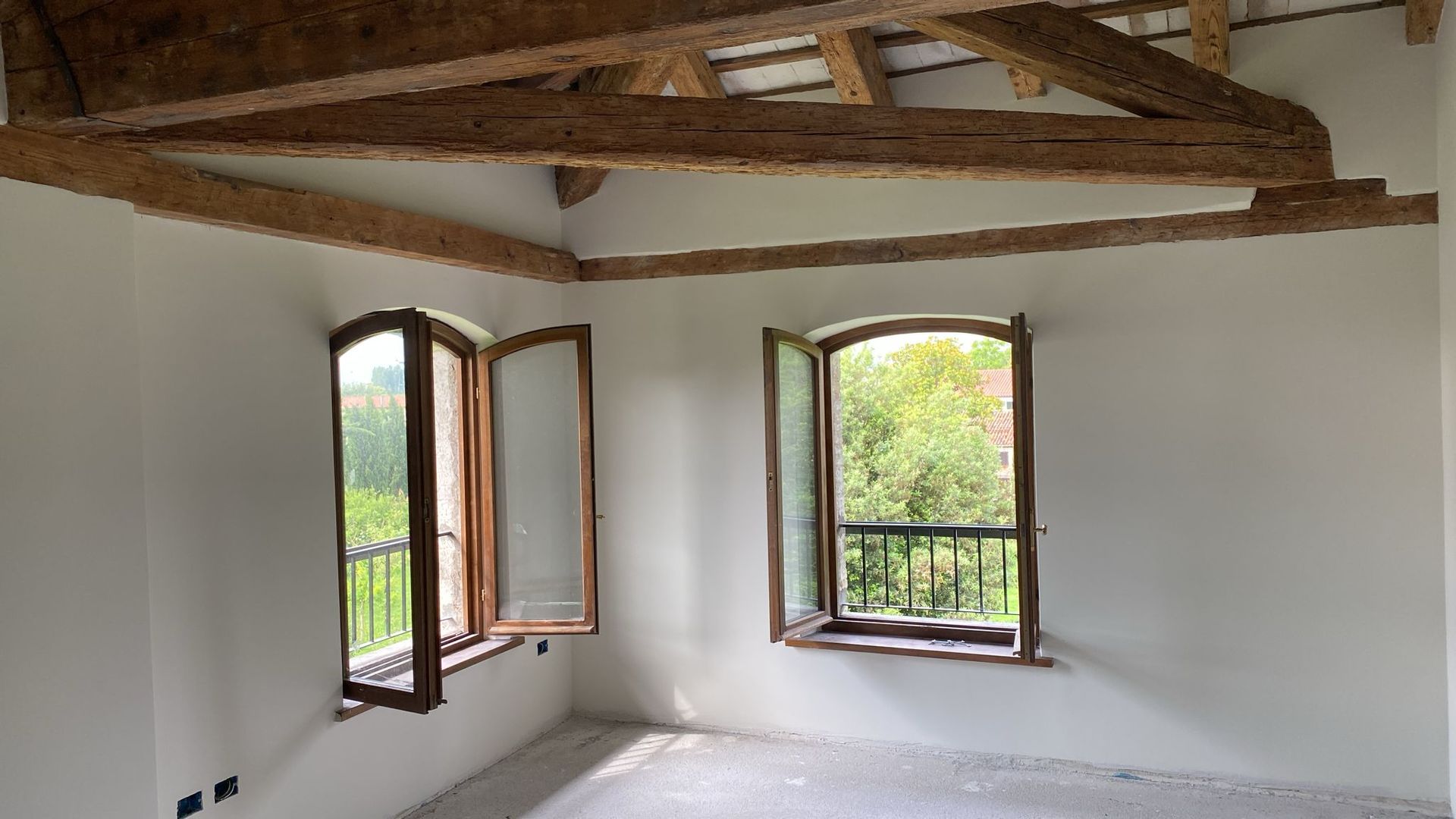 Una stanza vuota con due finestre e travi di legno sul soffitto.