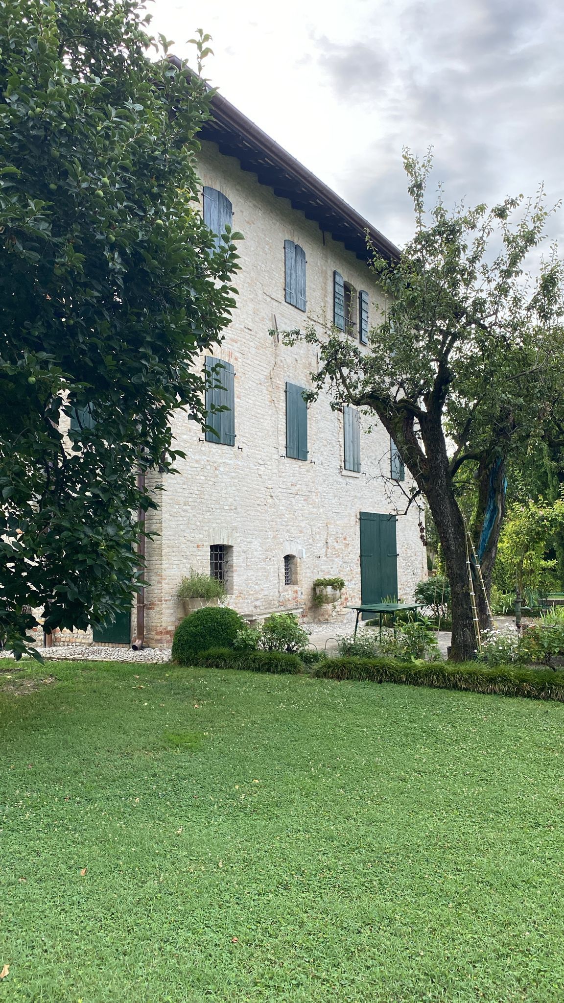 Un grande edificio bianco con le persiane verdi e un albero di fronte.