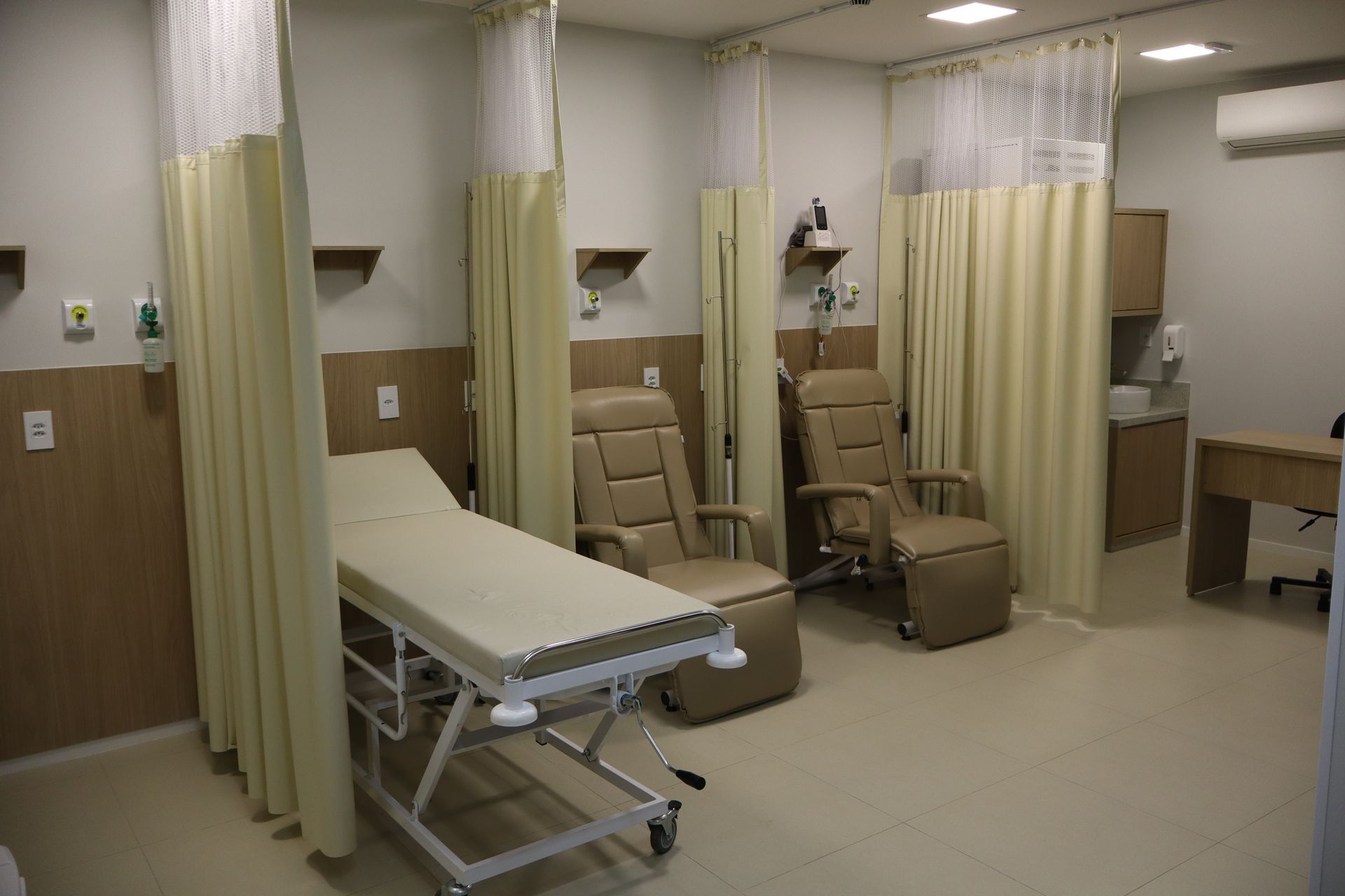 A hospital room with a bed , chairs and curtains.