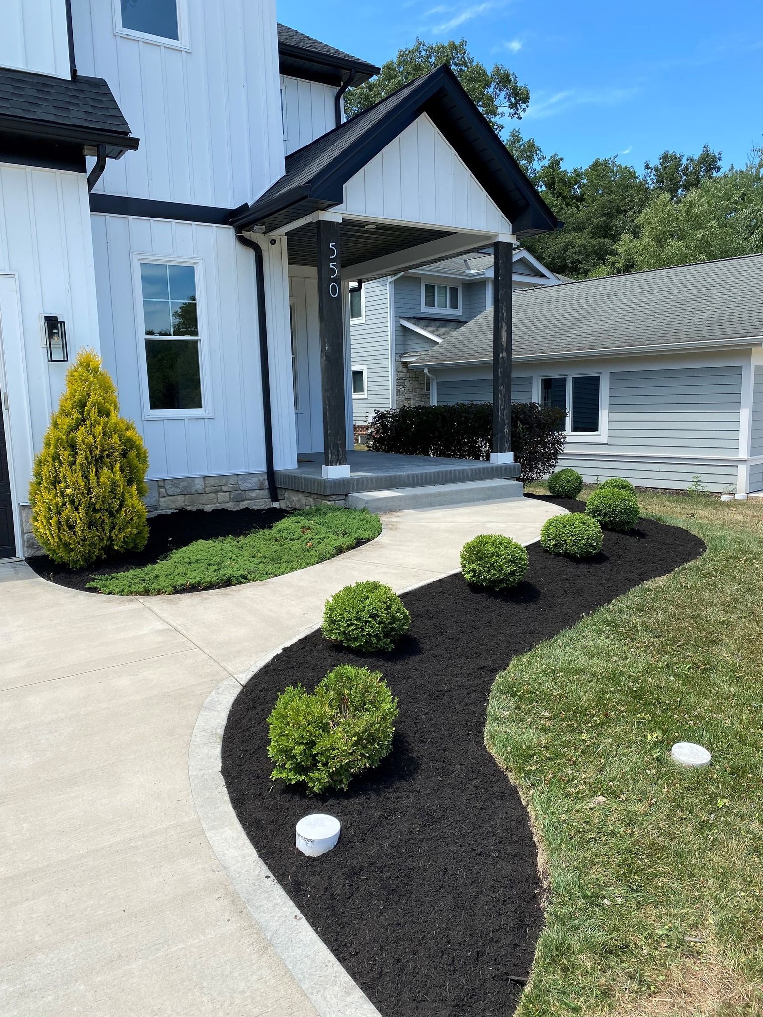 A modern house with a curving walkway and landscaping. Black mulch and green plants contrast the white exterior.