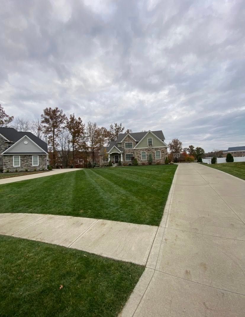 Suburban house with well-manicured green lawn and long concrete driveway under a cloudy sky.