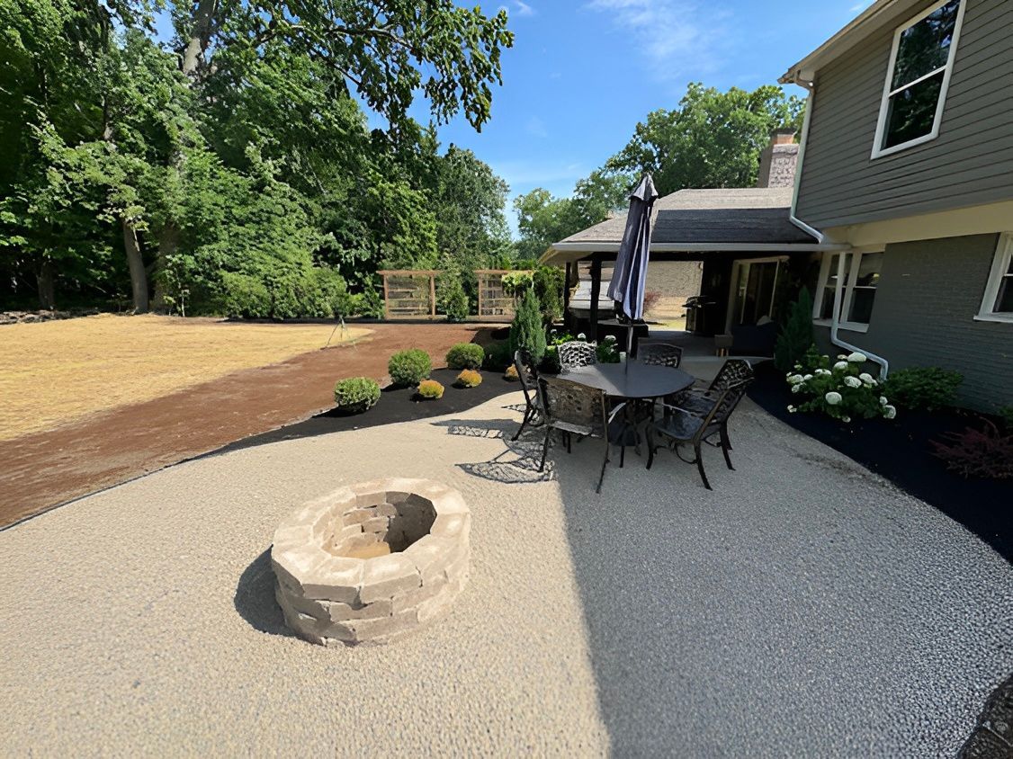 Backyard with gravel patio, fire pit, seating area with umbrella, and a house.