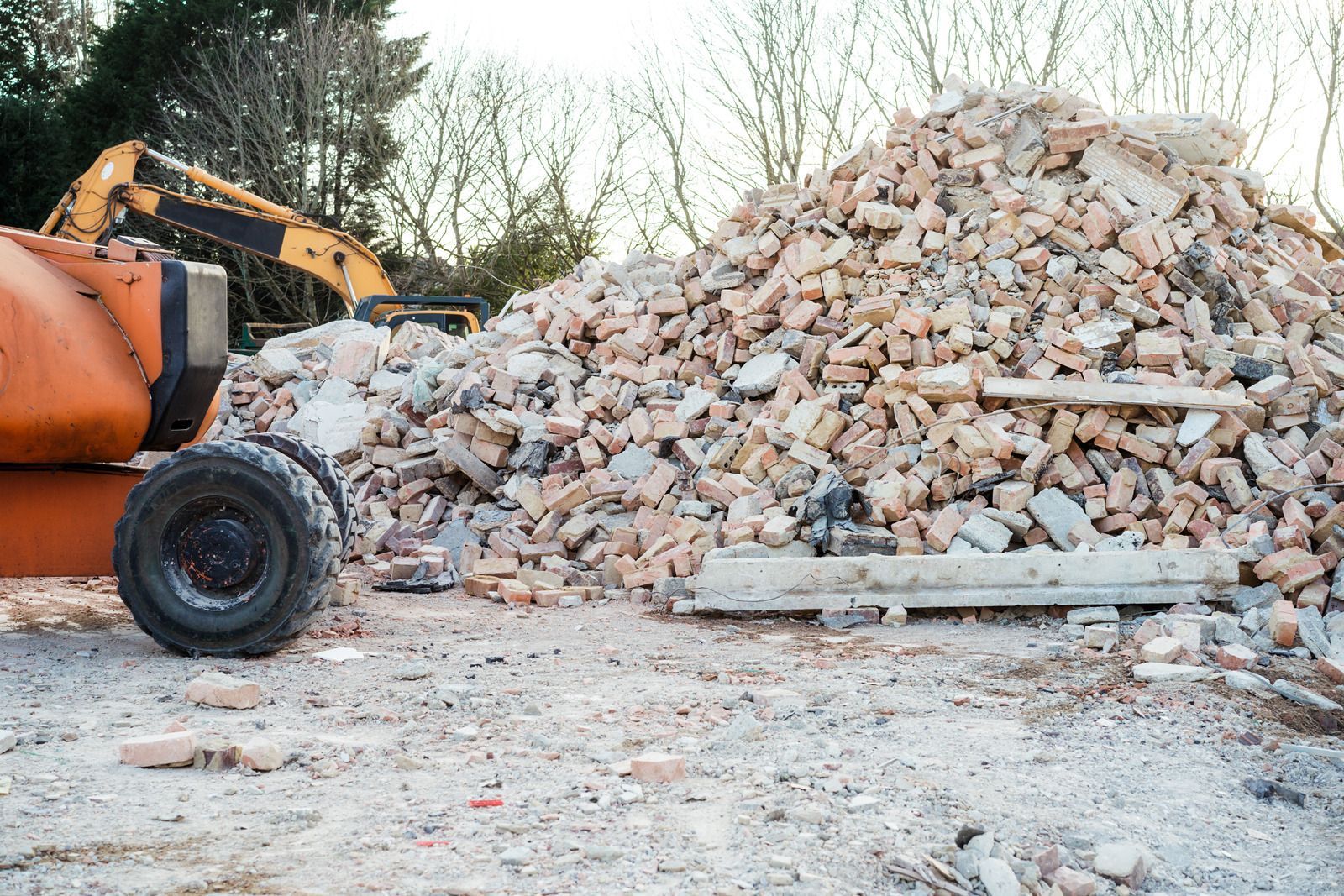 Orange excavator beside a large pile of rubble at a construction site